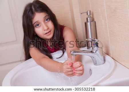 one beautiful 7-8 years middle eastern arab girl with red dress is washing her hands in the bathroom. looking at camera with smile. Developed from RAW. retouched with special care and attention.