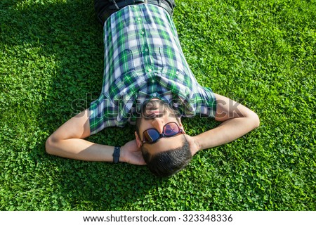 One fashion middle eastern man with beard, fashion hair style is resting on beautiful green grass day time. young arab businessman 20-30 years, resting after hard work. smart phone, tablet. looking