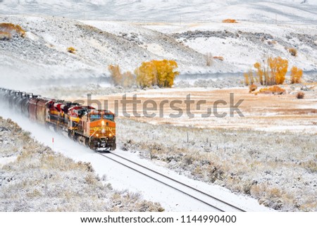 Train transporting tank cars. Season changing, first snow and autumn trees. Rocky Mountains, Colorado, USA.