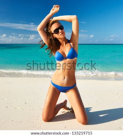 Woman in bikini at tropical beach sitting on her knees