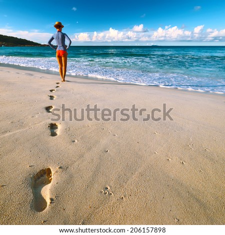 Woman at beautiful beach at Seychelles walking on sand. Focus on footprints.