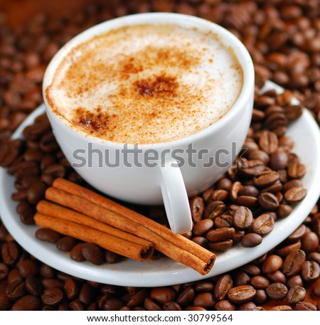 Cup of cappuccino  with cinnamon and spilled out coffee beans.