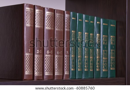 Close up of several volumes of  books on dark wooden shelf
