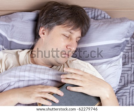 Portrait of sleeping man with book in bed