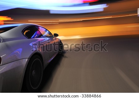 Silver car moving at speed under neon lighting