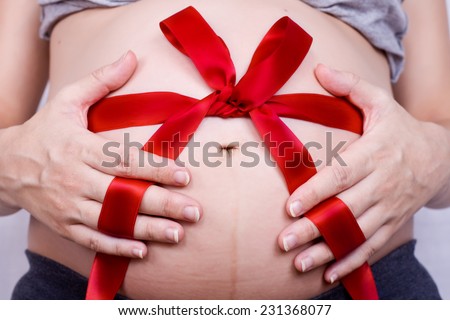 Pregnant woman holding hands with a red bow on her baby bump
