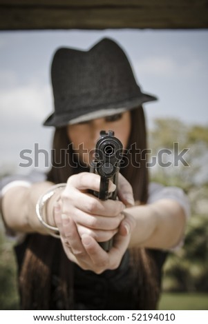 Beautiful woman with gray cap pointing a gun at the camera