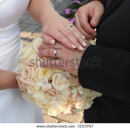 bride and grooms hands placed atop a bouquet of roses showing off wedding band set