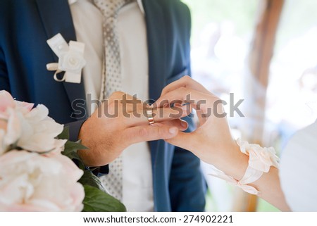 Hands of wedding couple putting golden rings to finger of each other.