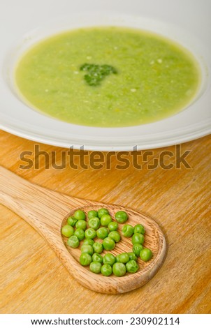 Fresh green pea soup in white soup plate. With wooden spoon full of green pea.