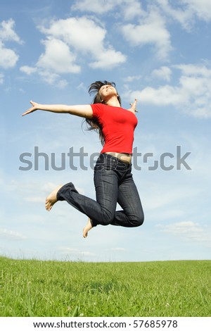 young beautiful girl in red shirt and with long brunette hair jumping at summer lawn