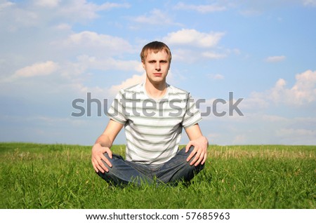 young man in jeans and white shirt with stripes sits at summer lawn, hands on knees, looking at camera