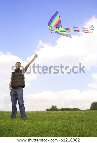 young man standing on summer lawn and playing with multicolored kite, looking at camera