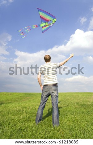 young man standing on summer lawn and playing with multicolored kite, view from back