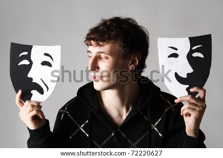 young man holding two emotion theater masks, looking on sad mask