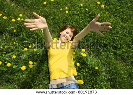 young girl in yellow shirt lying on grass, smiling and stretching her hands to camera