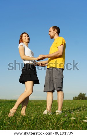 young man in yellow shirt and redhead girl standing on summer lawn and holding for hands, full body