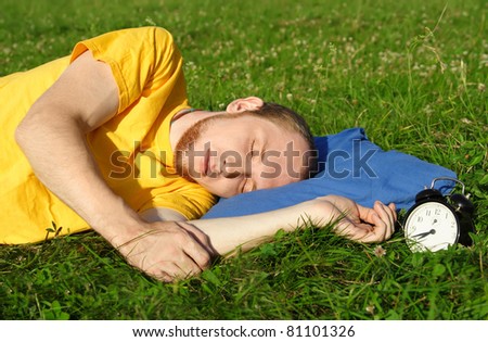 man in yellow shirt sleeping on summer meadow near clock, lying on side, rest concept