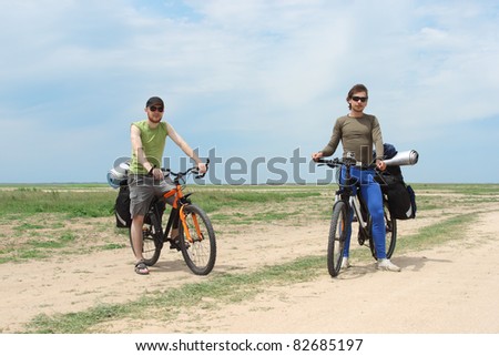 two bicycle tourists standing on road, blue sky and horizon