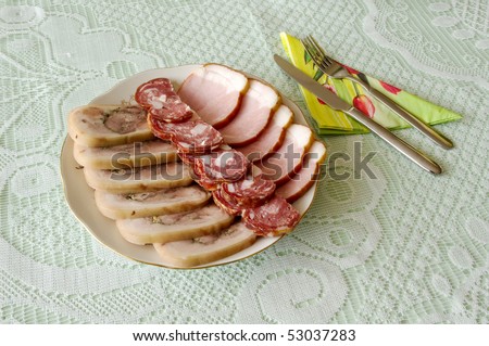 Cutting sausage and cured meat on a celebratory table knife and fork with green napkin.
