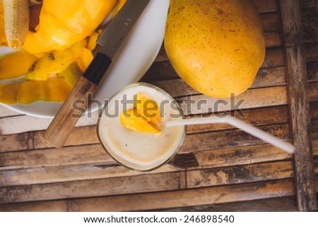 freshness fruit mango  lying on a white plate with knife. Fresh shake with shape heart love  mango slices milk and straw on brown board rustic