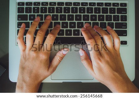 A woman\'s hands are typing on a laptop computer keyboard. The monitor is visible in the image, but it is not clear what she is working on.