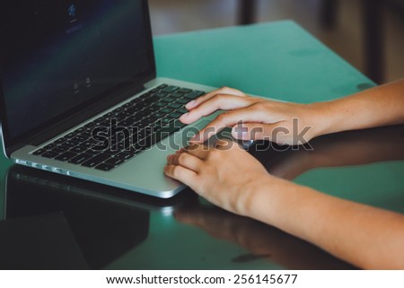 A woman\'s hands are typing on a laptop computer keyboard. The monitor is visible in the image, but it is not clear what she is working on.