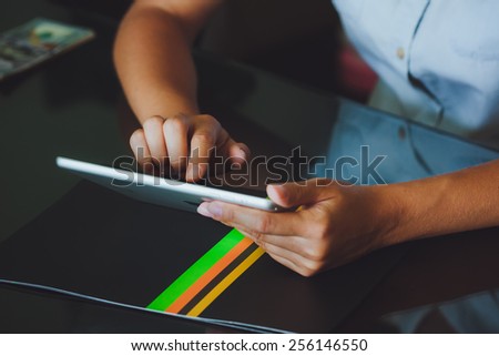 hand belonging to a woman holds a large tablet while the other hand uses a pointer finger to access something on the tablets touch screen display. The tablet has a gray case and a glass screen.