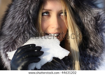 face beauty girl with blonde hair outdoors, in a fur coat, eats snow