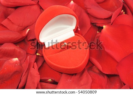 box with a gold wedding ring with a diamond is in the petals of red roses