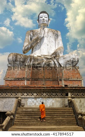 A giant Buddhist statue and a monk in Cambodia. An unidentifiable lone Buddhist Monk walks up the stairs towards the big Buddha. You can easily isolate the sky and put your own in.