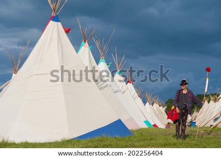 GLASTONBURY, UK - JUNE 28: A festival goers stands by a row of tipi tents at Glastonbury Festival on 28th June, 2014 at Pilton Farm, Somerset.