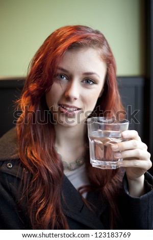 Beautiful young woman with red hair sitting in a restaurant drinking water.