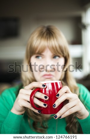 Portrait of a young woman staring straight making an ugly face while holding a cup of coffee.