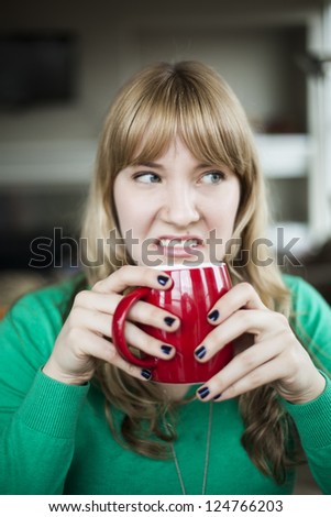 Portrait of a young woman staring straight making an ugly face while holding a cup of coffee.