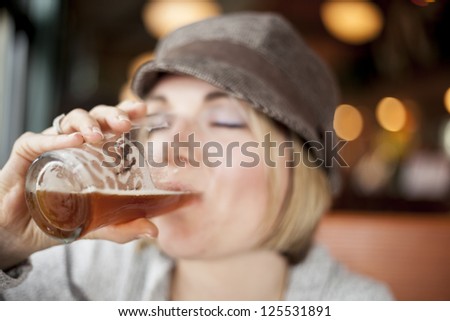 Young woman in cute brown hat drinking a beer.