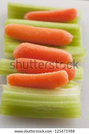 Delicious celery stalks and carrots on white plastic cutting board.