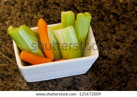 Delicious celery stalks and carrots on white plastic cutting board.