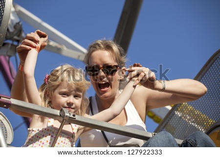 Beautiful, blonde-haired mother and daughter on a ride at the amusement park.