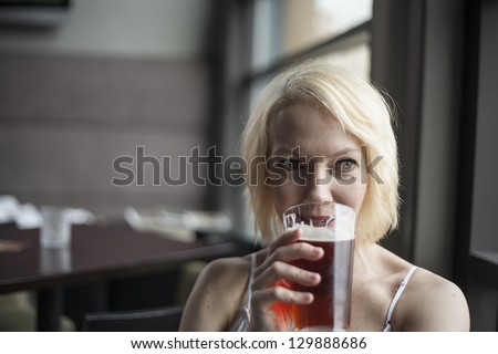 Portrait of a blonde woman drinking a glass of pale ale.