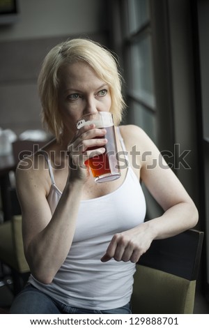 Portrait of a blonde woman drinking a glass of pale ale.