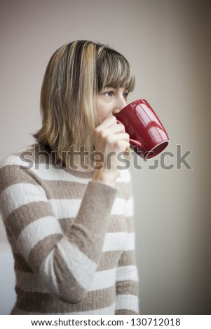 Portrait of a beautiful young woman with blonde hair drinking coffee from a red mug.