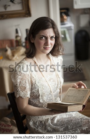 Portrait of an angry young woman in a vintage white wedding dress reading a book.