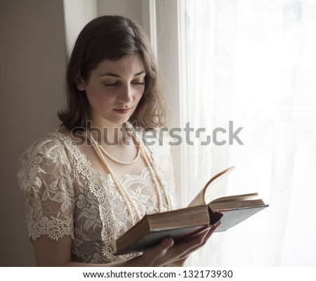 Portrait of a young woman in a vintage white wedding dress reading a book.