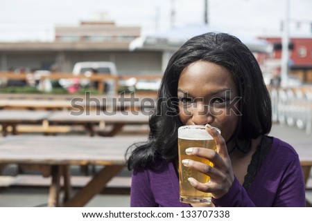 Young African American woman drinks a pale ale from a pint glass.