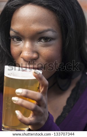 Young African American woman drinks a pale ale from a pint glass.