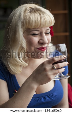 Portrait of a beautiful young woman with blond hair drinking a glass of wine and laughing.