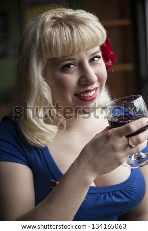 Portrait of a beautiful young woman with blond hair drinking a glass of wine and laughing.