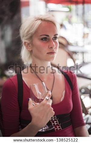 Portrait of a beautiful blond woman shot outdoors at a cafe. She has green eyes and bleached blond hair and is holding a glass of white wine.