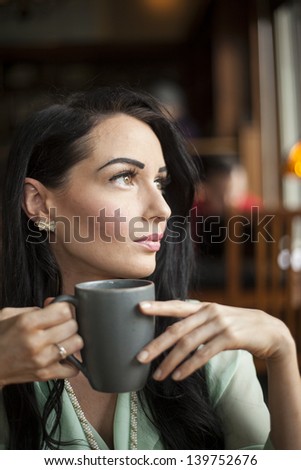 Beautiful young woman with dark brown hair and eyes holding a gray coffee cup.